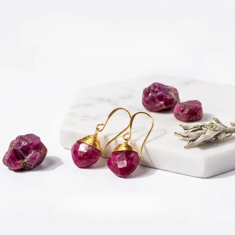 Gold earrings with pink gemstones on a white surface