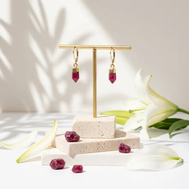 Gold earrings with red gemstones on a gold stand with white flowers in the background