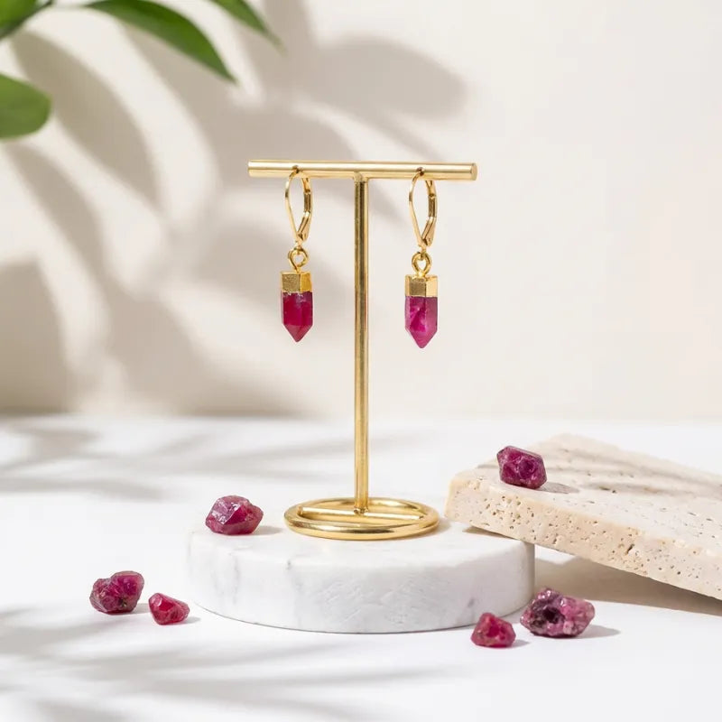 Gold earring stand with pink gemstone earrings on a light background