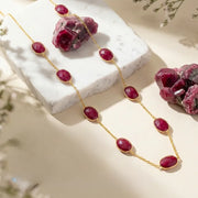 Gold necklace with red gemstones on a marble surface with red stones.