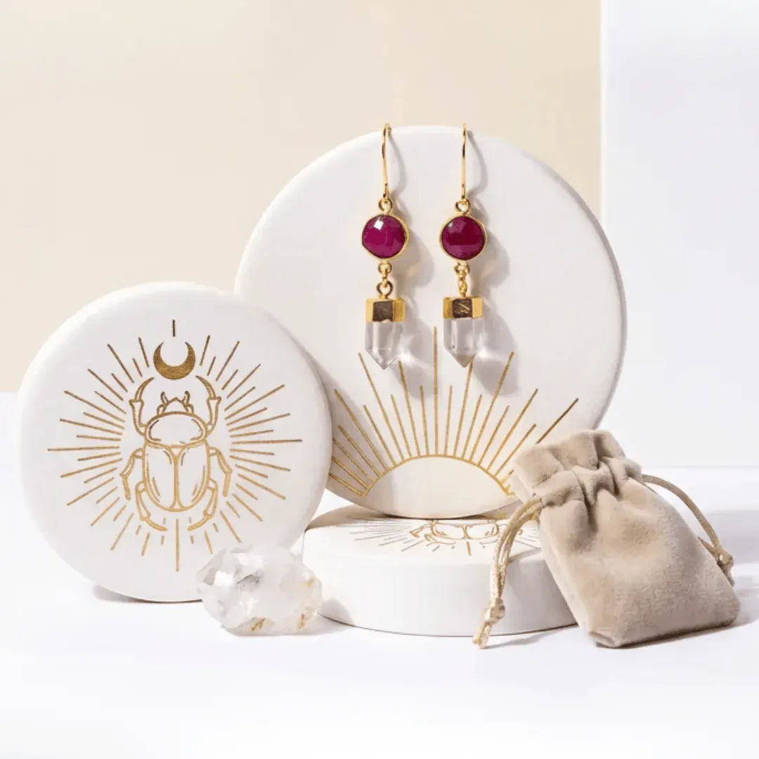 Jewelry set with earrings on a decorative stand, accompanied by a pouch and crystal on a light background.