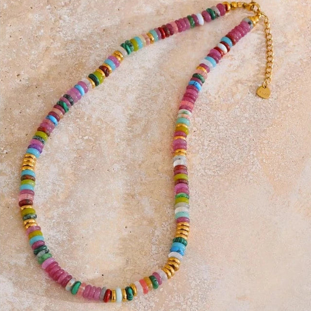 Colorful beaded necklace on a textured beige surface with motivational quote.