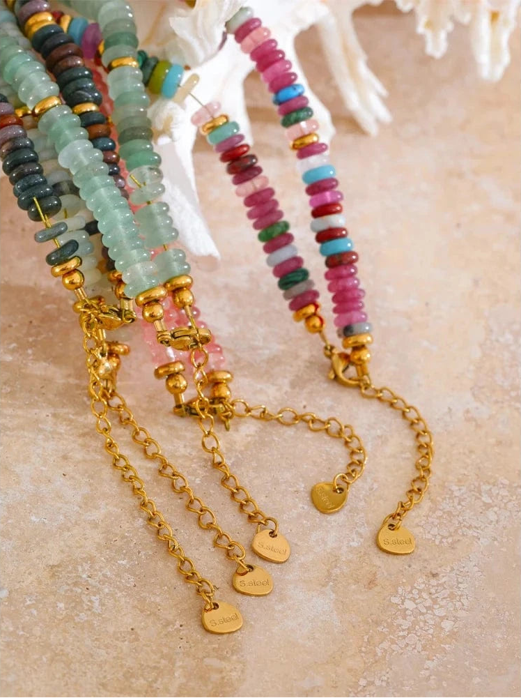 Colorful beaded bracelets with gold chains on a textured beige surface