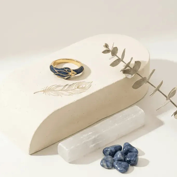 Gold ring with blue stones on a white stone surface with decorative elements
