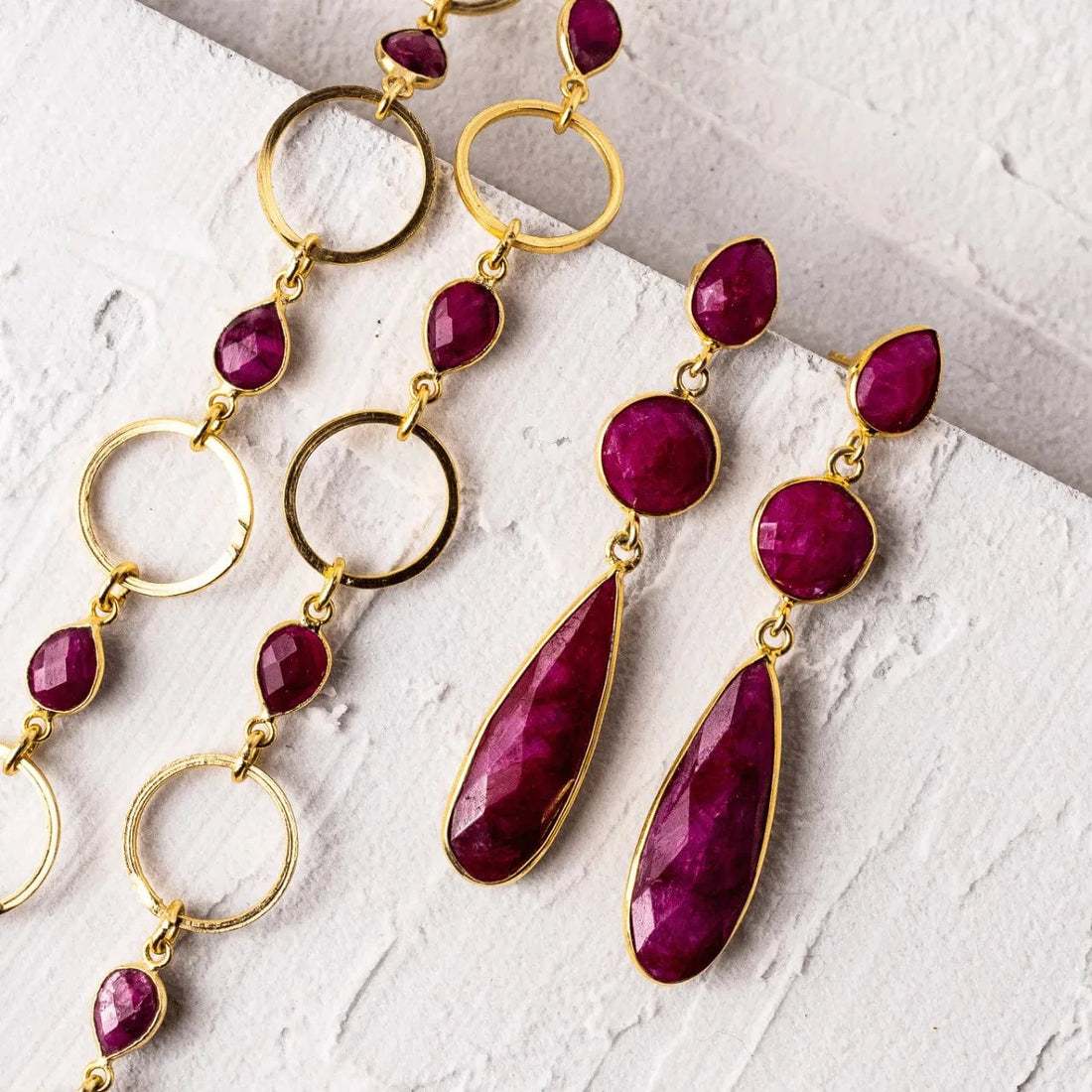 Gold and red gemstone earrings on a textured white surface