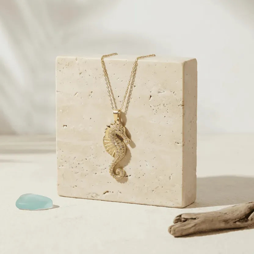 Gold seahorse necklace on a beige stone block with a natural setting