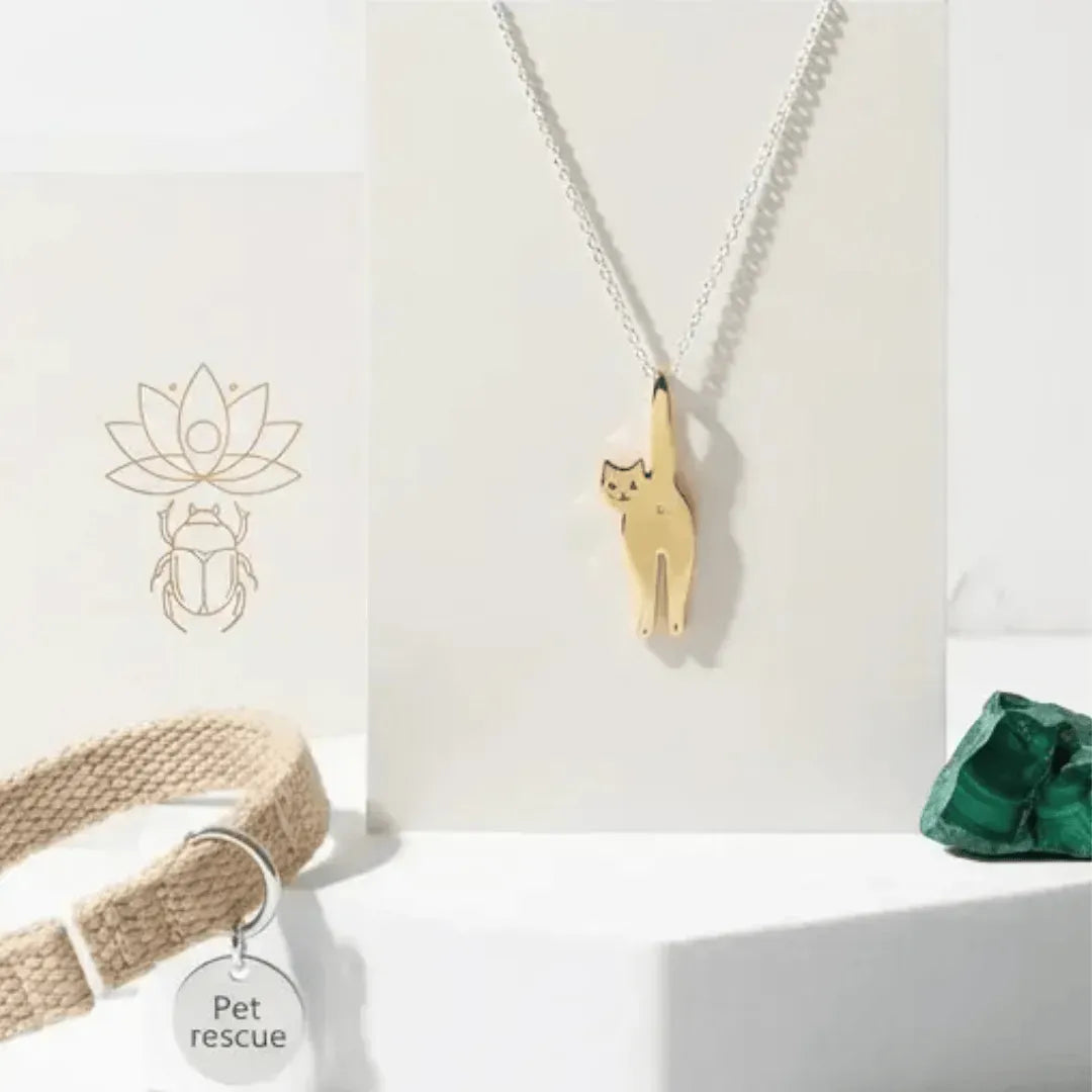 Gold cat-shaped pendant on a chain with a pet tag and green stone on a white background