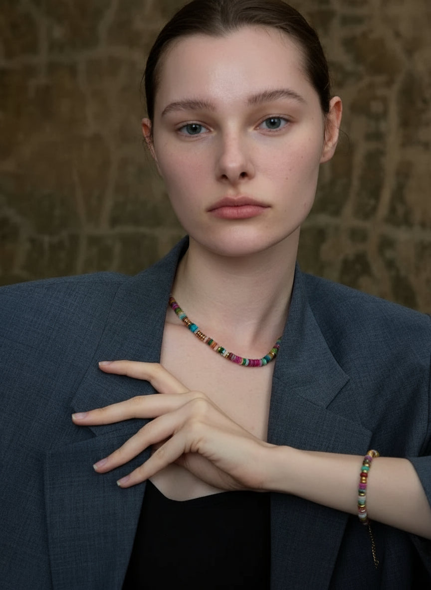 Woman wearing a dark blazer and colorful beaded necklace against a textured wall.