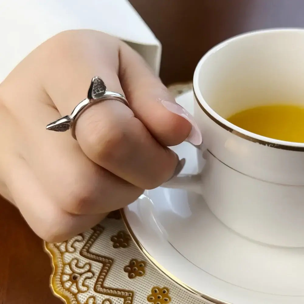 Sterling silver cat ears ring worn on a hand holding a cup of tea, highlighting its unique design and craftsmanship.