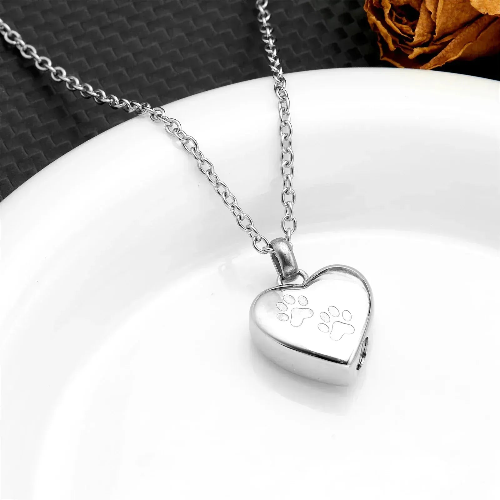 Silver heart-shaped pendant with paw prints on a white surface