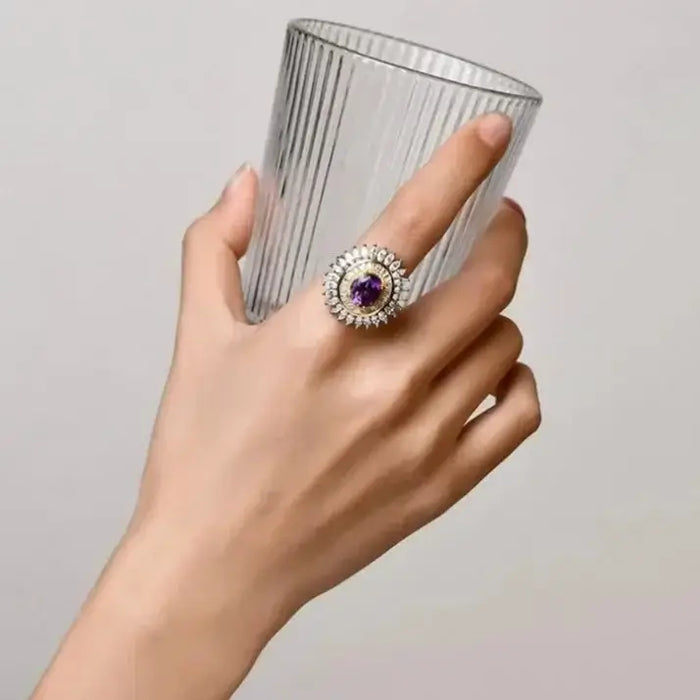 Hand holding a glass while wearing an Amethyst Sunflower Ring set in 925 sterling silver, showcasing its elegance.