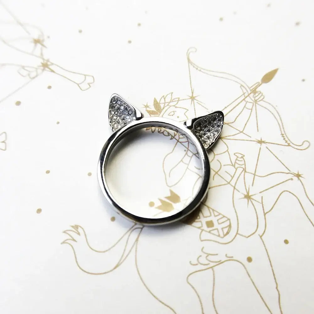 Sterling silver cat ears ring with sparkling zircon accents on a light patterned background.