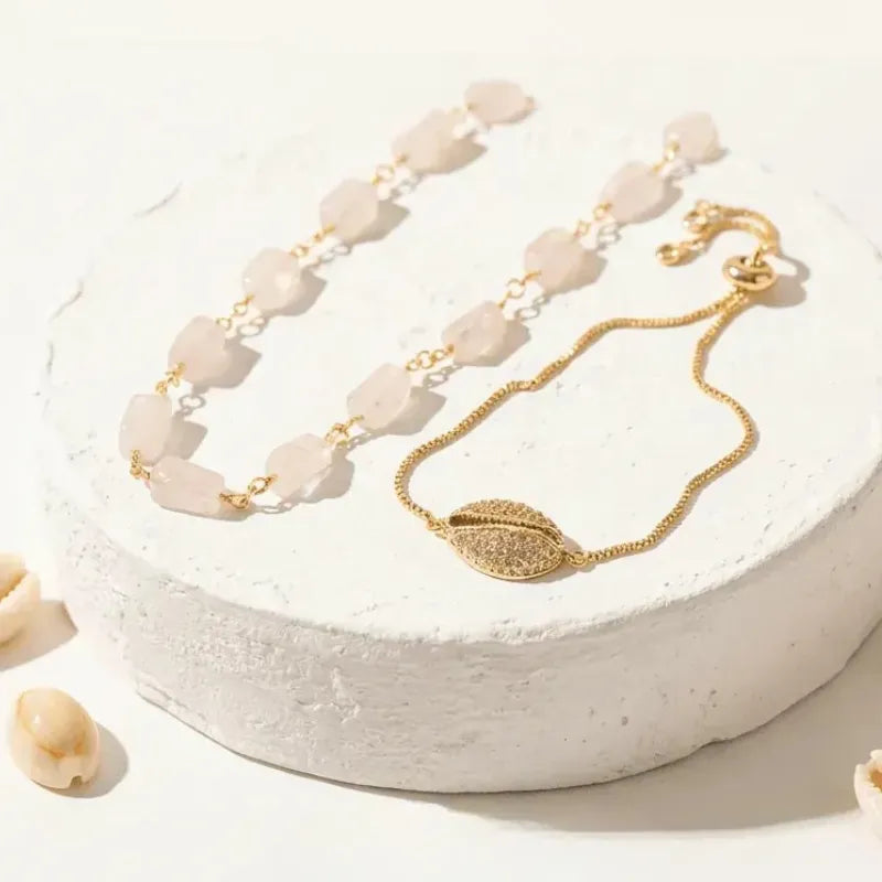 Gold bracelet with leaf charm on a white stone surface