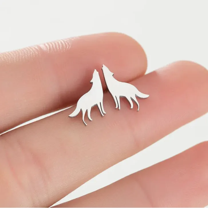 Silver wolf-shaped earrings held between fingers on a white background