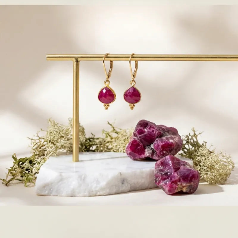 Ruby earrings on a gold stand with ruby stones on a marble base.