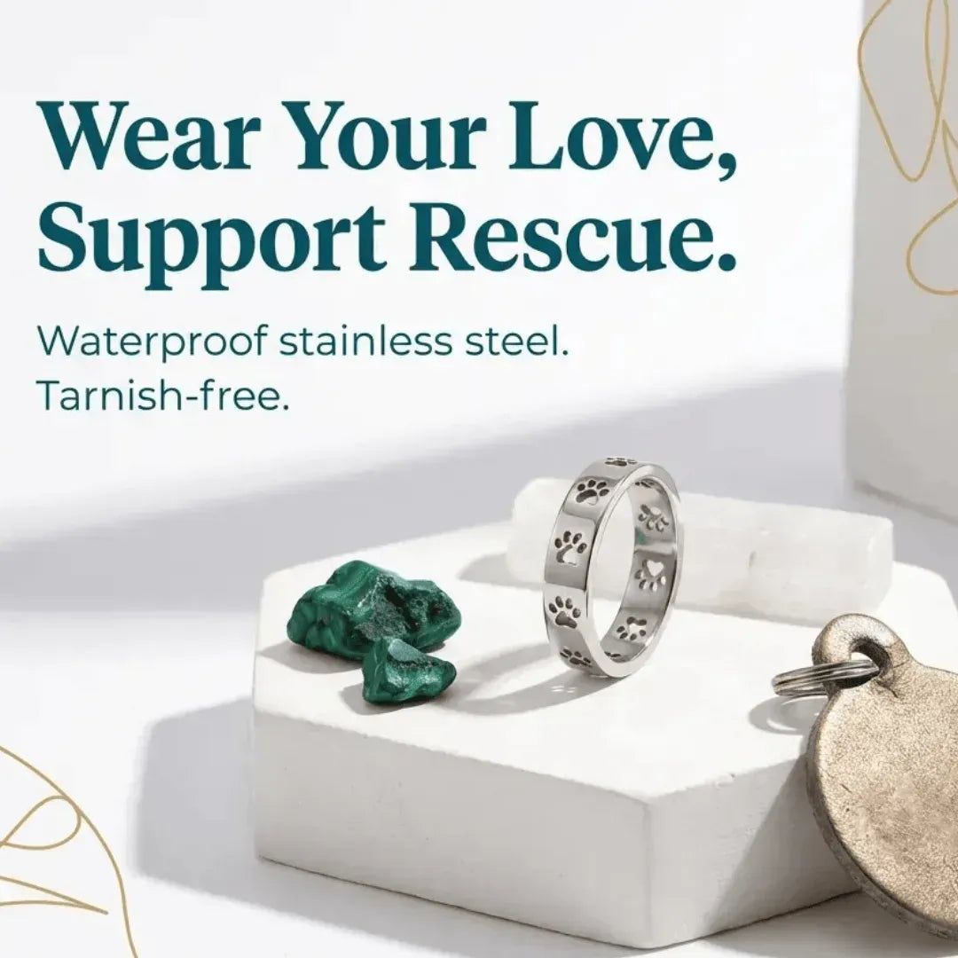 Silver ring with paw print design on a white platform with green stone and dog tag, text 'Wear Your Love, Support Rescue'.