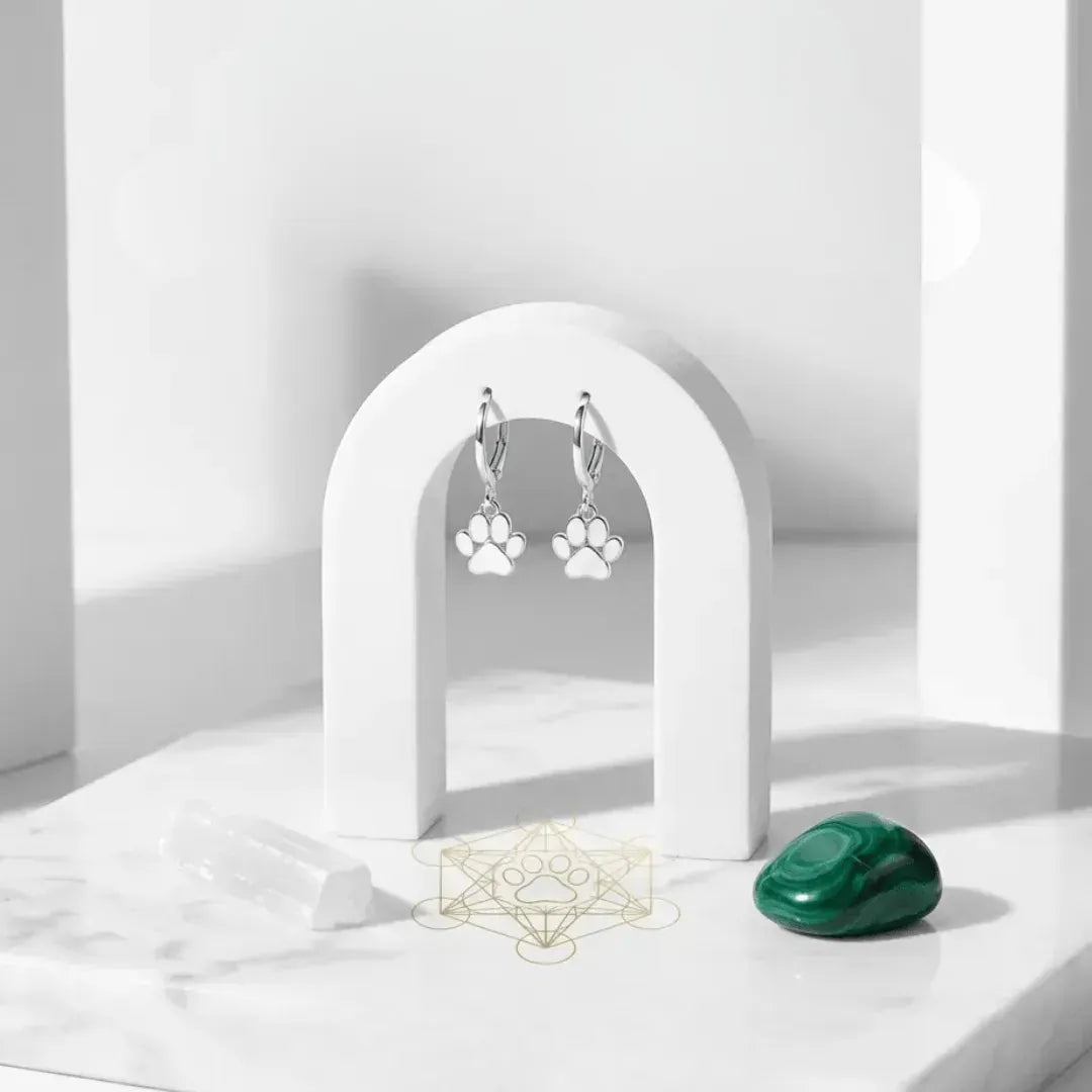 Paw print earrings on a white arch stand with a green stone on a white surface.
