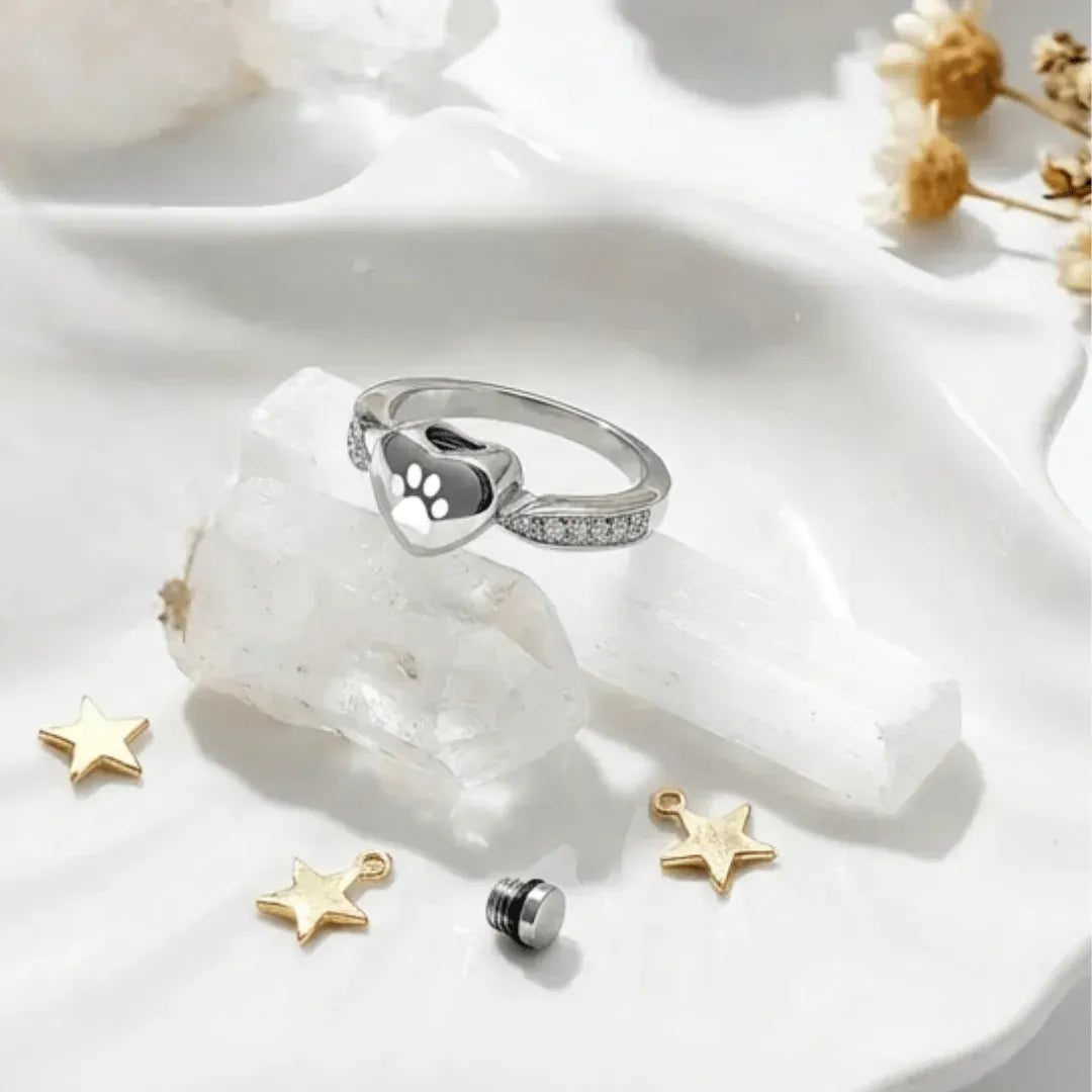 Silver ring with paw print design on a white stone surface with decorative stars.