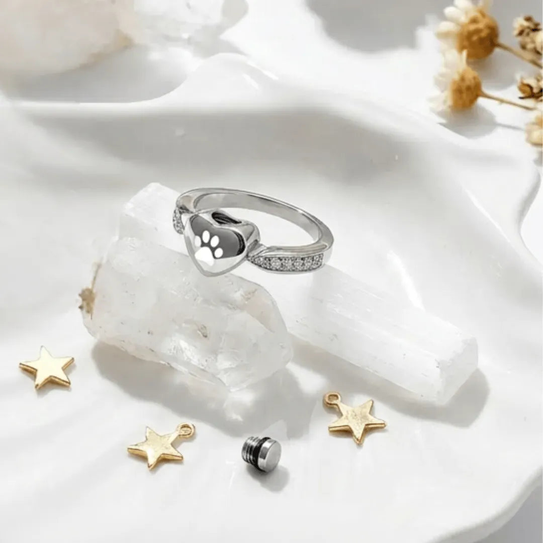 Silver ring with paw print design on a white stone surface with decorative stars.