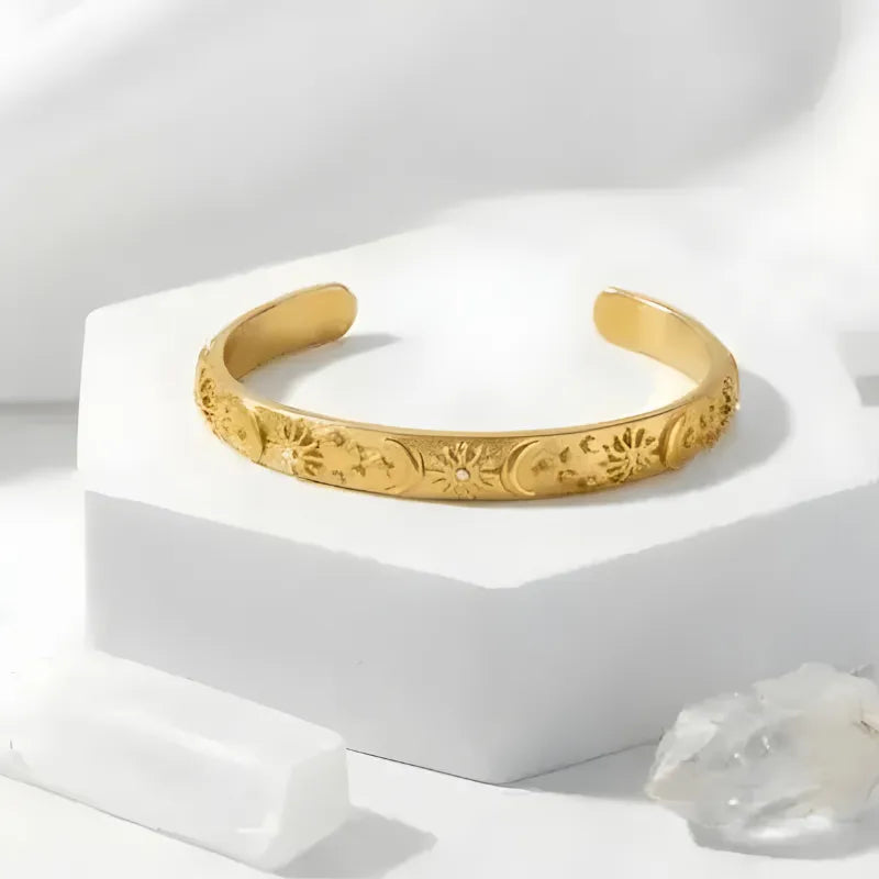 Gold bracelet with intricate designs on a white pedestal