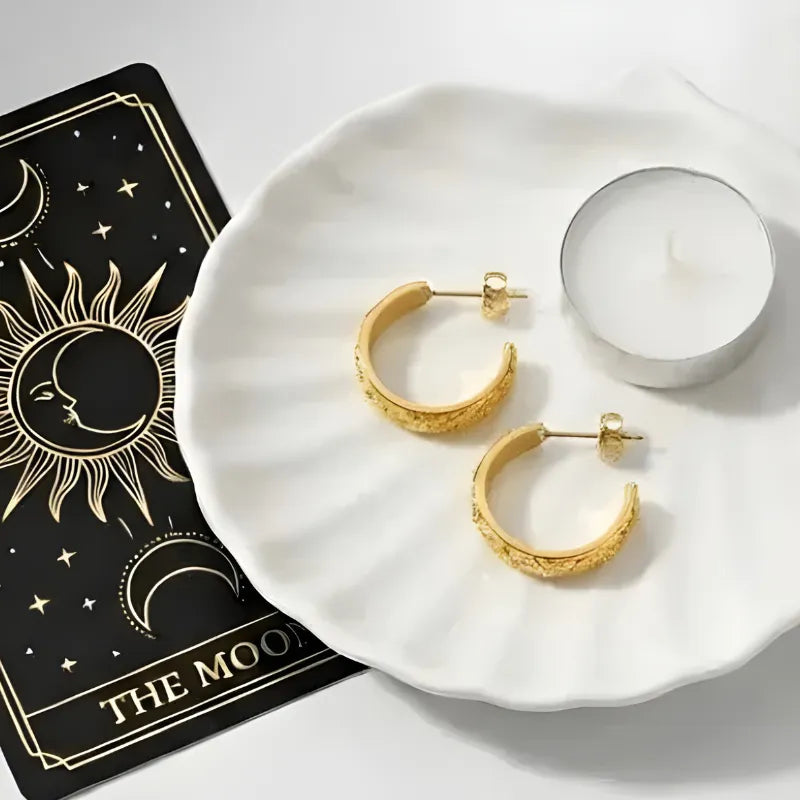 Gold hoop earrings on a white plate with a tarot card and candle in the background