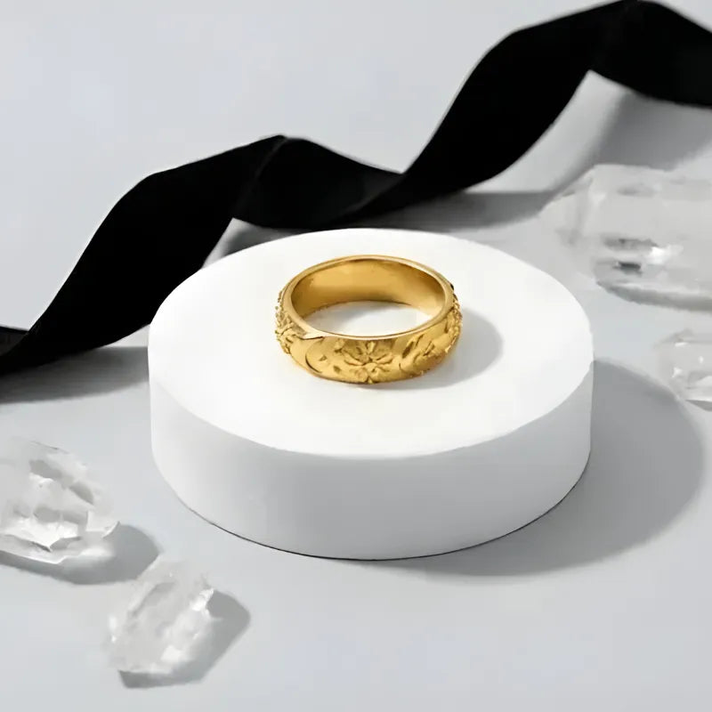 Gold ring on a white pedestal with black ribbon and crystal objects in the background