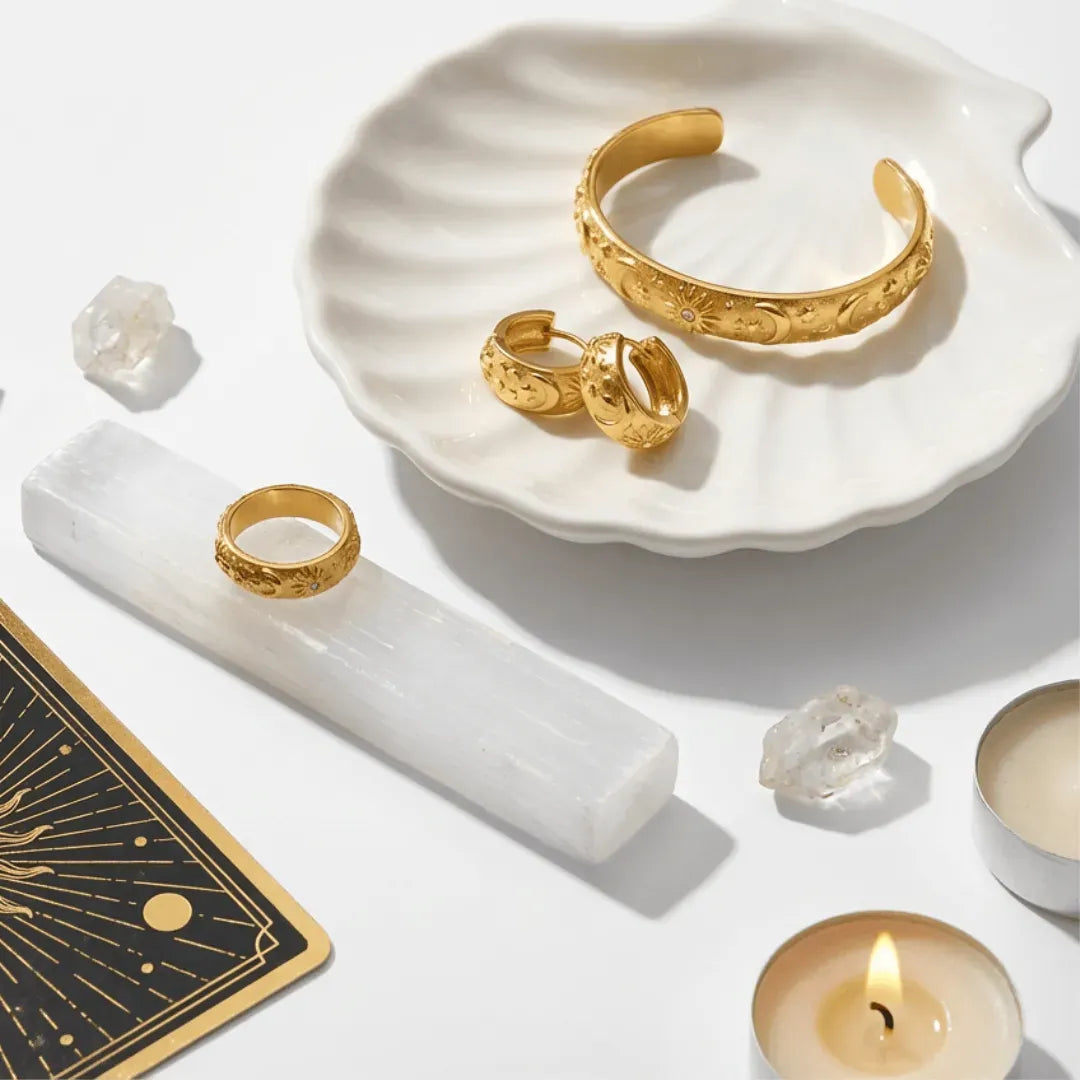 Gold jewelry on a white dish with candles and crystals on a white background