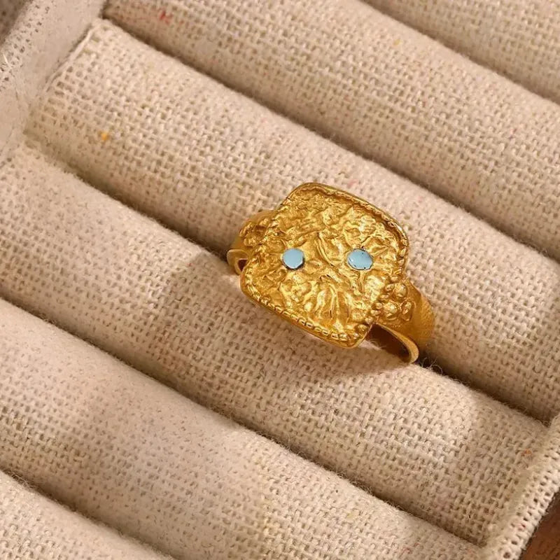Gold ring with turquoise stones on a textured beige surface