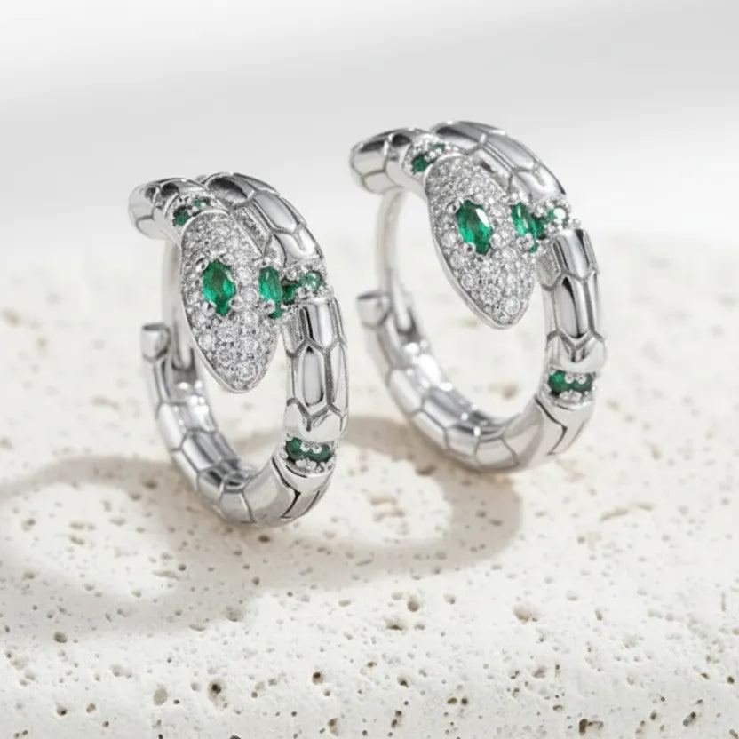 Gold hoop earrings with green gemstones on a textured white surface
