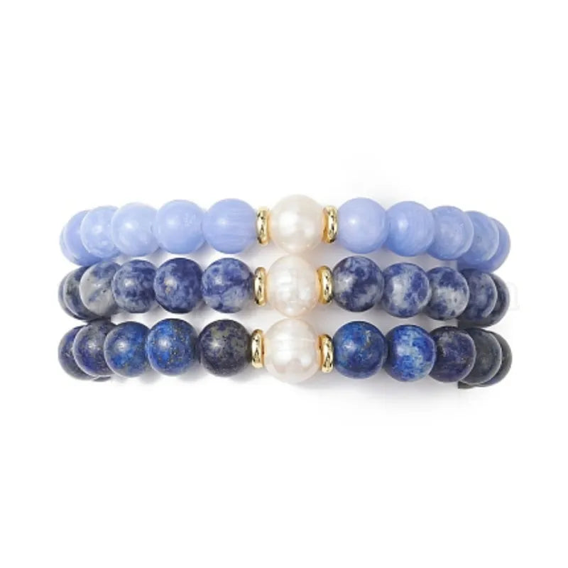 Three blue gemstone pearl bracelets on a stone tray by the water