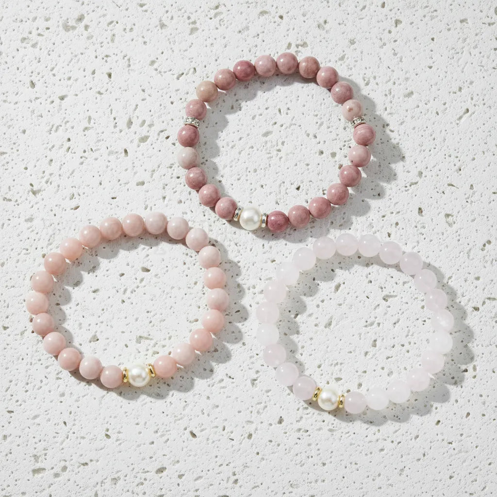Three pink beaded bracelets with gold accents on a light blue background