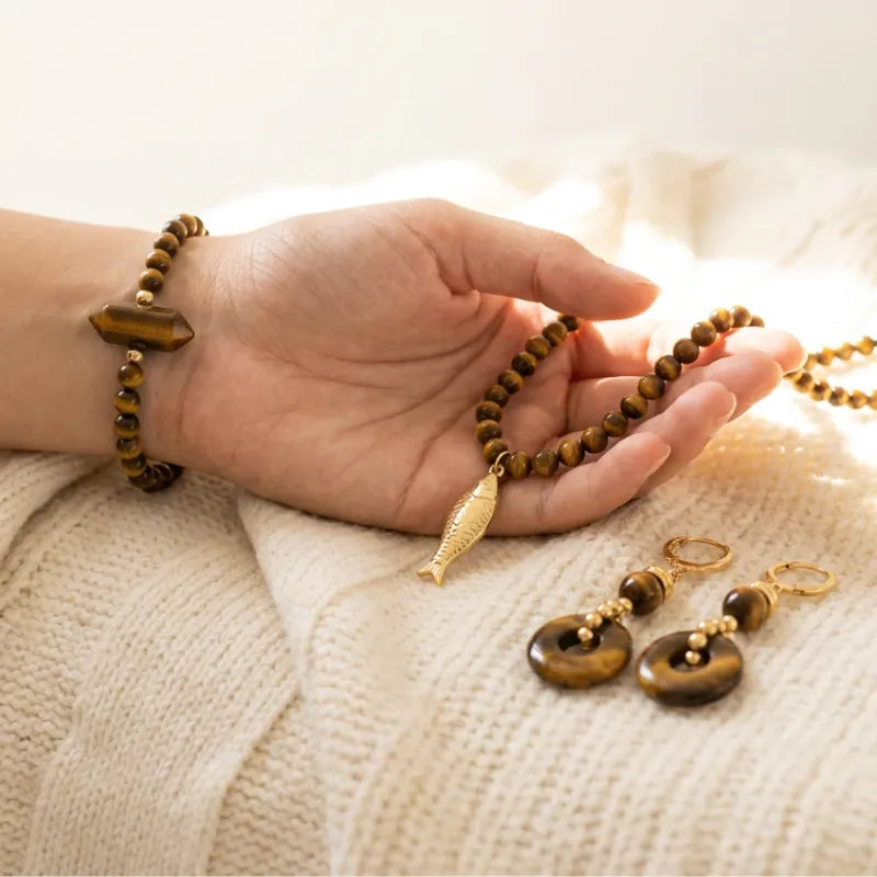 Hand holding a beaded necklace with matching earrings on a textured surface