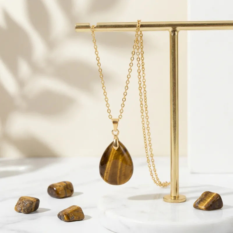 Gold necklace with a tiger's eye pendant on a gold stand with stones on a light background