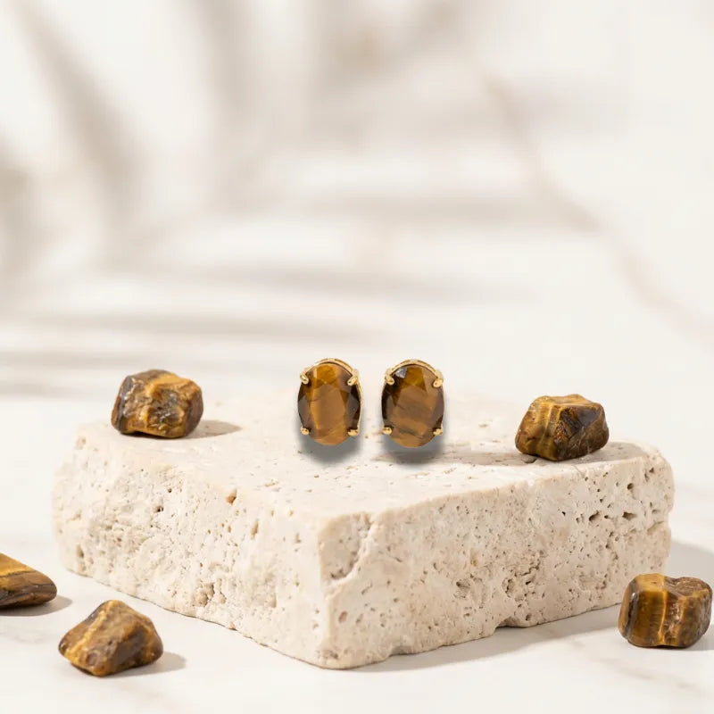 Tiger's eye stud earrings on a stone platform with scattered stones on a neutral background