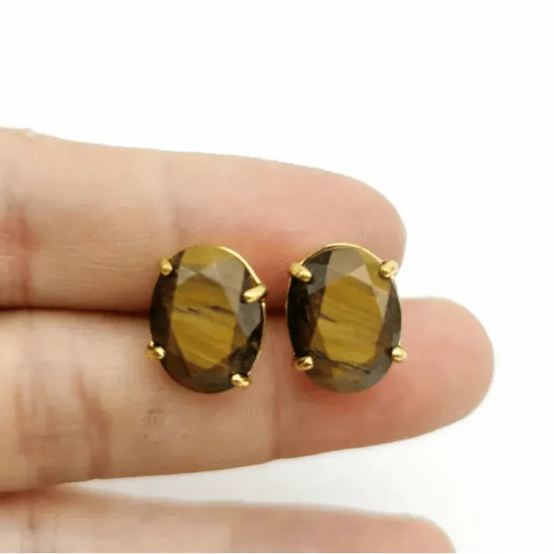 Gold earrings with smoky green gemstones held between fingers on a white background