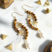 Gold and brown beaded earrings on a marble surface with geometric shapes.