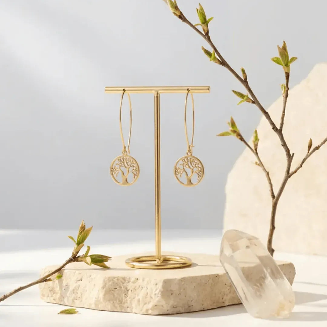 Gold tree-shaped earrings on a stand with a natural stone and branch background