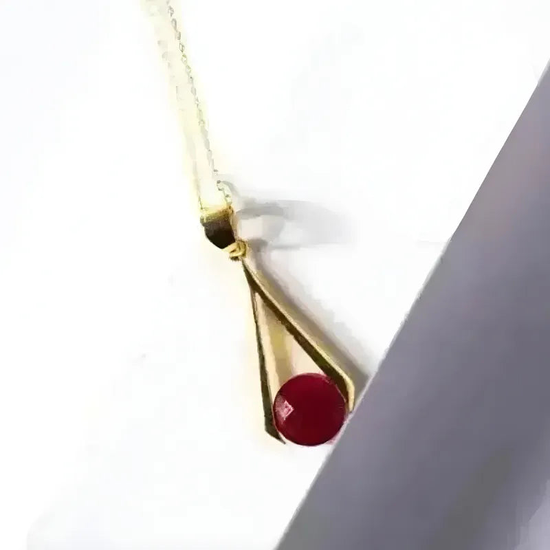 Gold necklace with a red gemstone on a white background