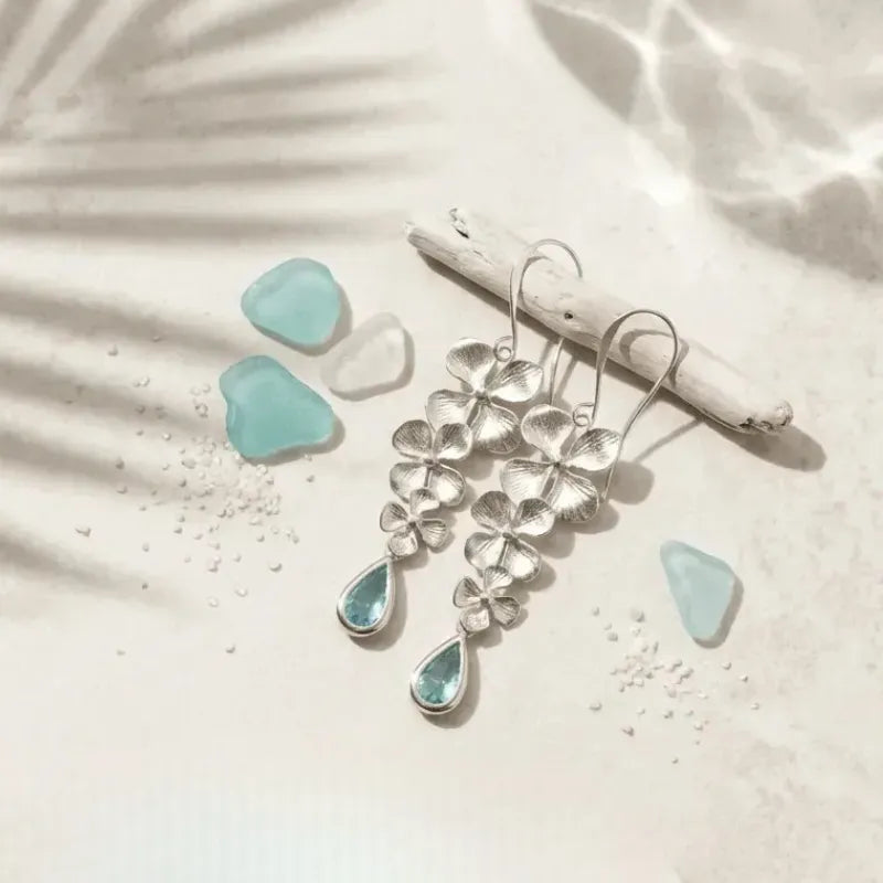Silver earrings with teardrop-shaped gemstones on a sandy background