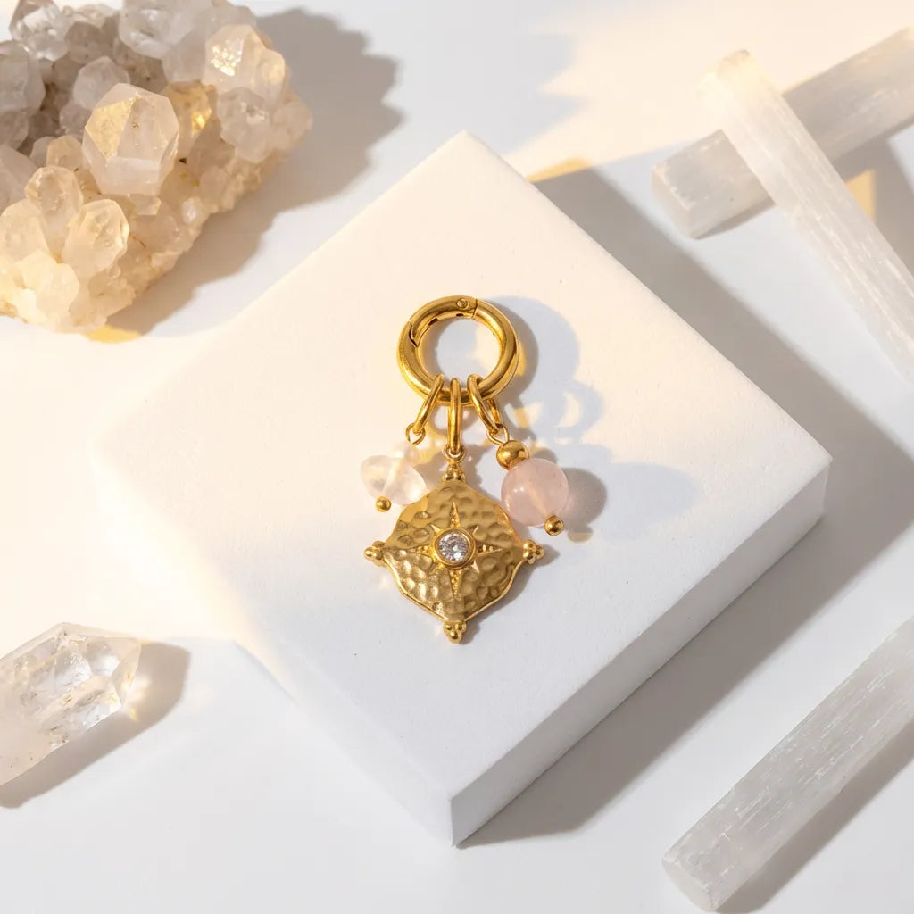 Gold pendant with pink beads on a white stand with crystals in the background