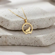 Gold necklace with a wolf pendant on a stone surface