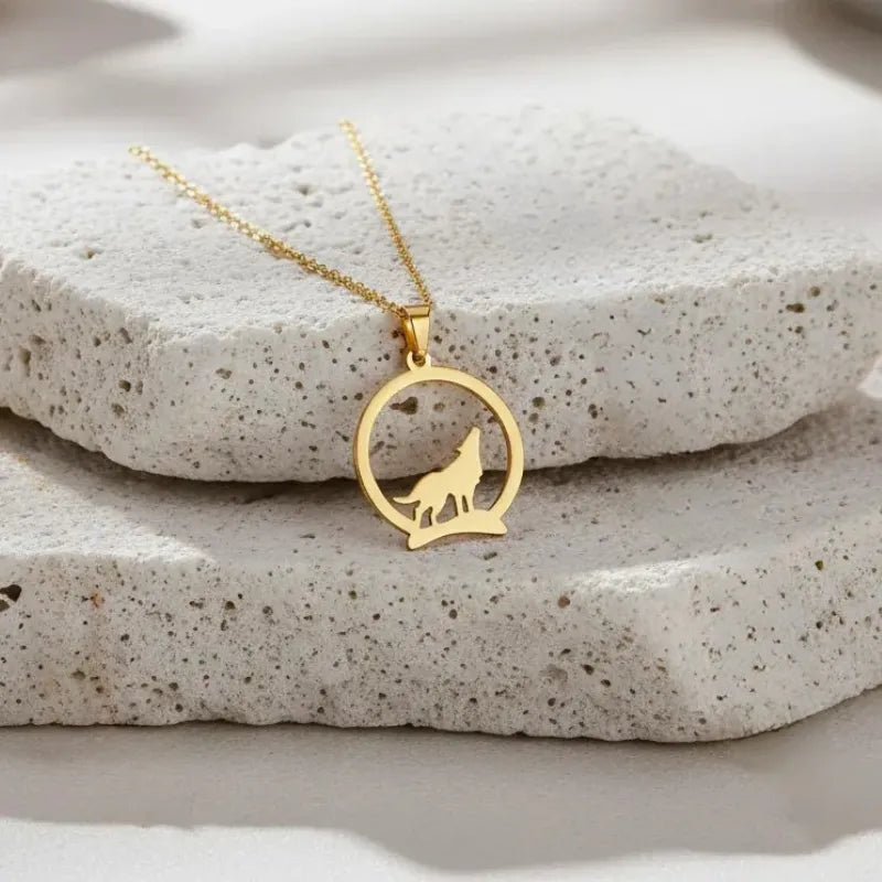 Gold necklace with a wolf pendant on a stone surface