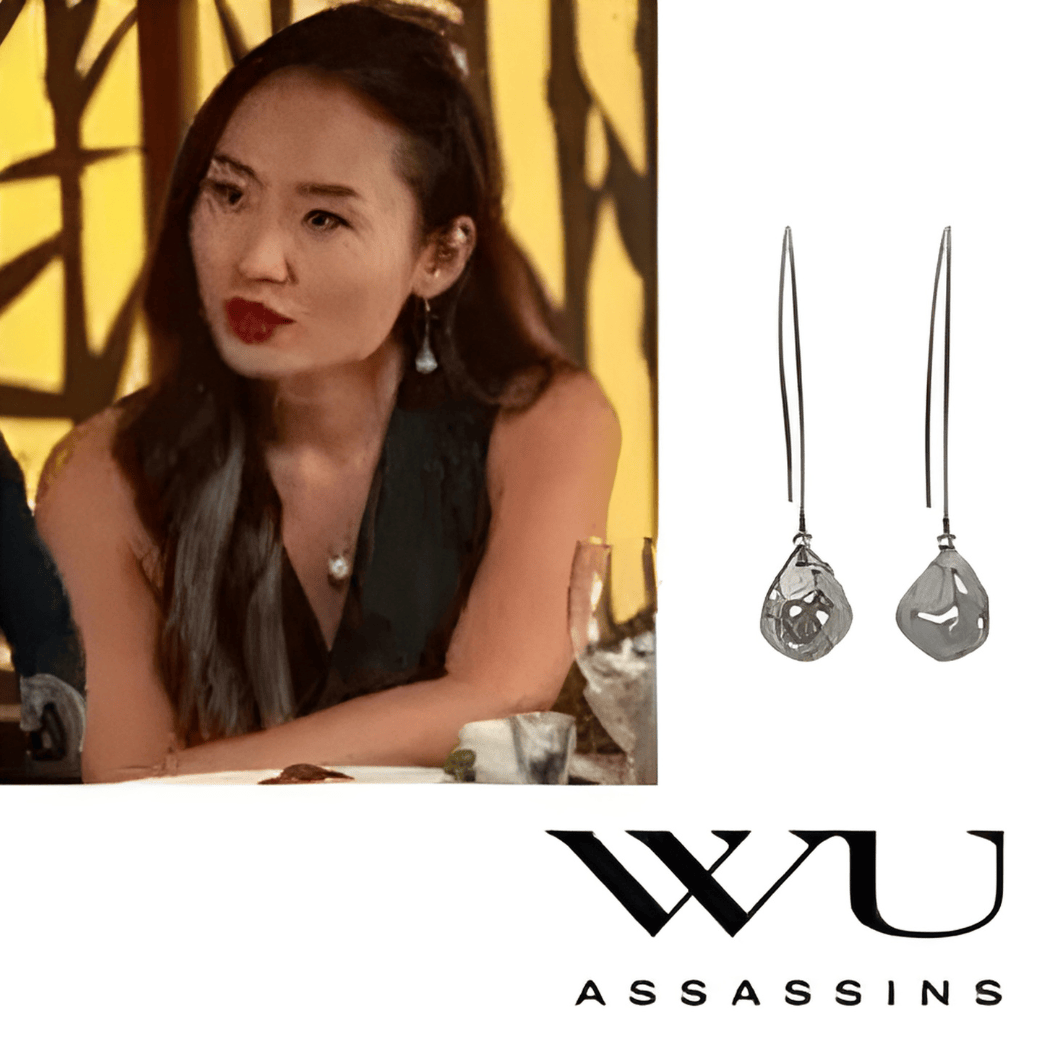 Woman sitting at a table with earrings displayed next to her, featuring the WU Assassins brand.