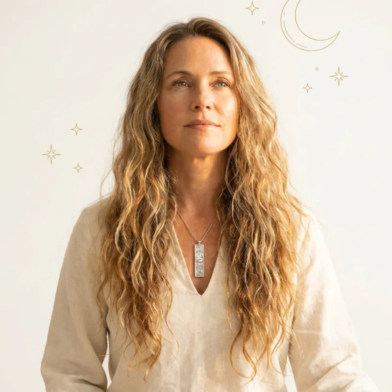 Woman with long wavy hair wearing a necklace against a light background
