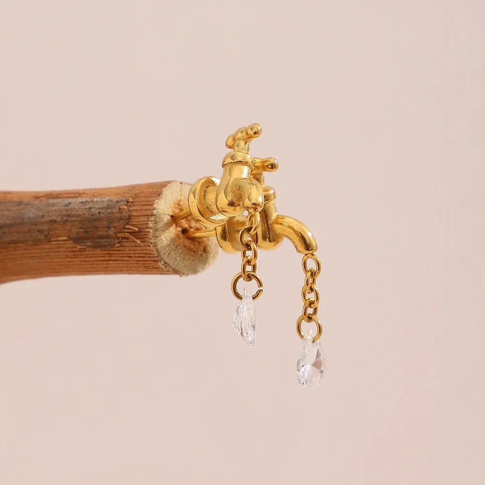 Gold faucet with water droplets attached to a wooden branch on a beige background