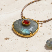Agate pendant in an asymmetrical gold frame with a red accent stone, on a rope chain