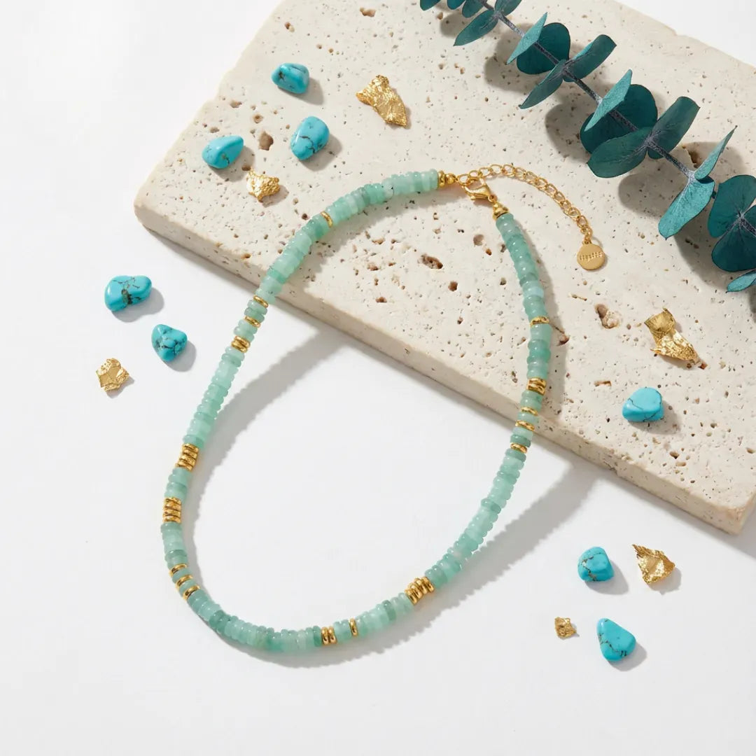 Turquoise beaded necklace with gold accents on a textured surface with scattered turquoise stones and gold leaves.