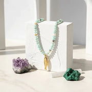 Necklace with a gold pendant on a white block, surrounded by crystals on a light background