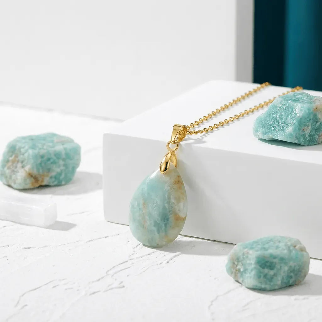 Teardrop-shaped pendant with gold chain on a white surface with turquoise stones.