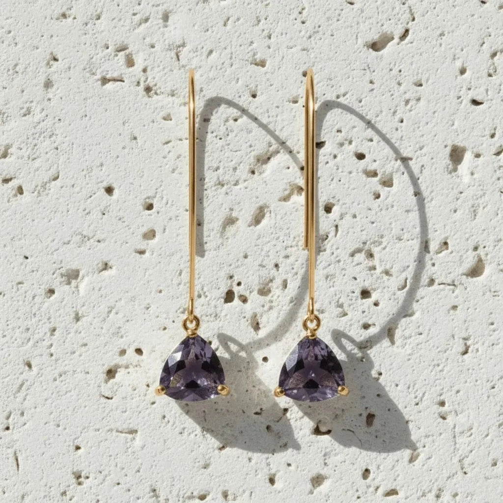 Gold earrings with purple gemstones on a textured beige surface